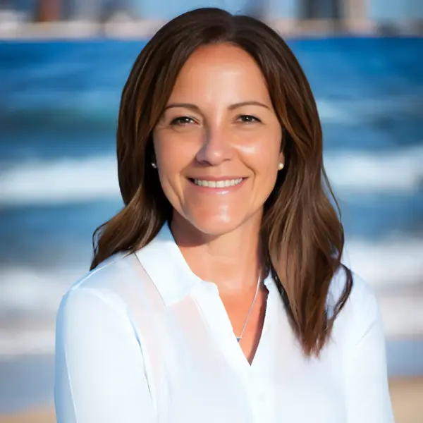 Isabel Peace smiling in a white shirt by the beach, with ocean waves and a city skyline behind her.